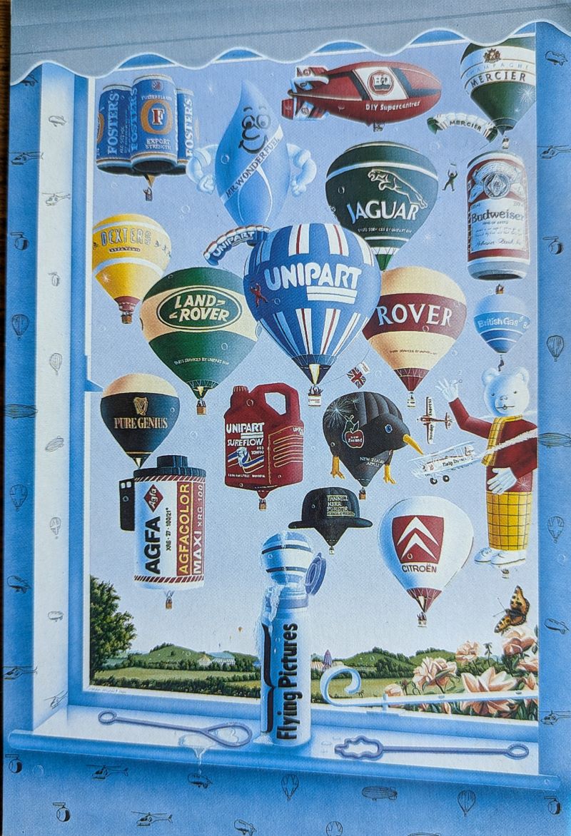 A colour post card of a painting of 18 balloons and an airship in a blue sky viewed through an open window with a small tube of bubble mixture on the sill bearing the words Flying Picture
